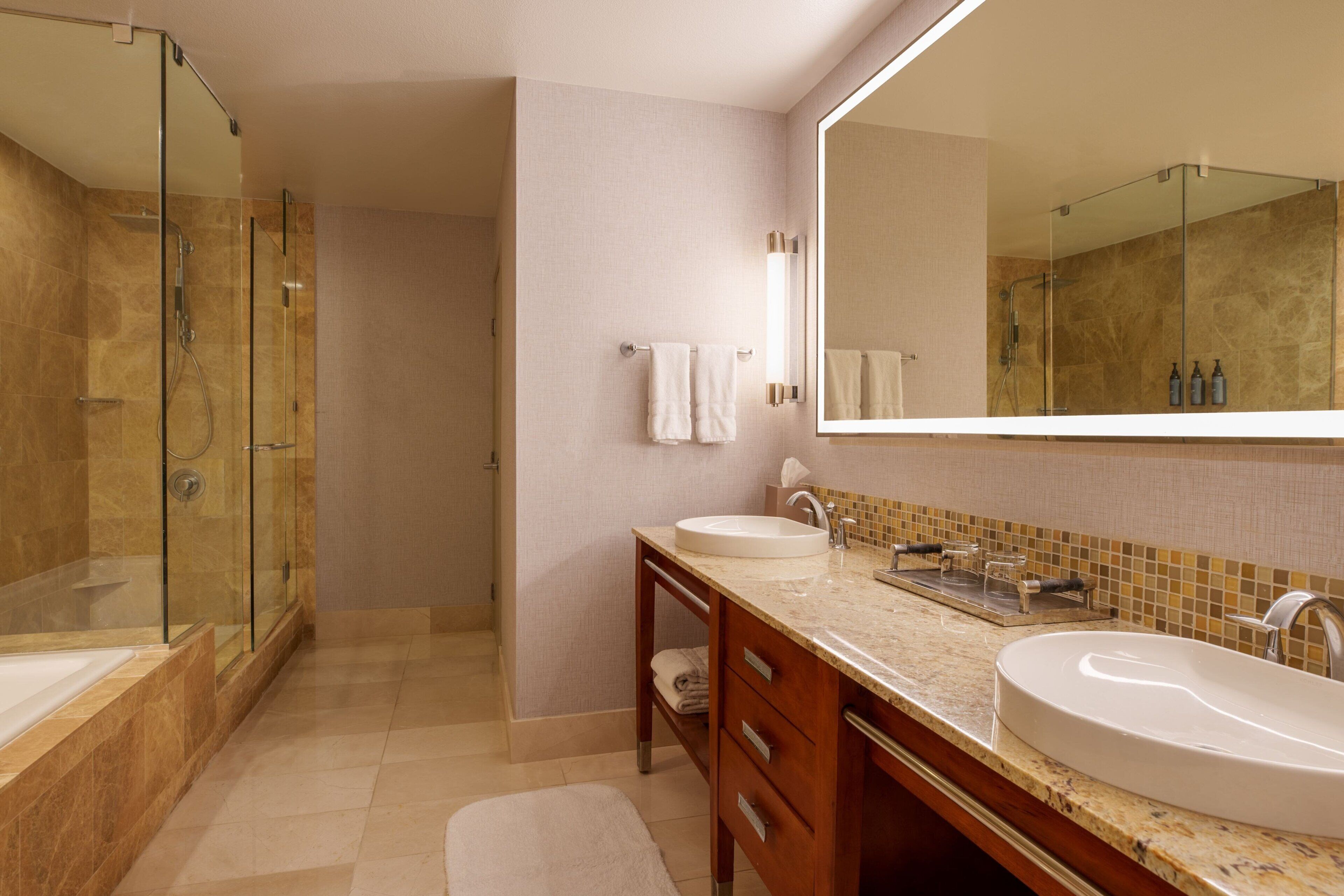 Un baño moderno con ducha envuelta en vidrio, un espejo grande y dos lavamanos.