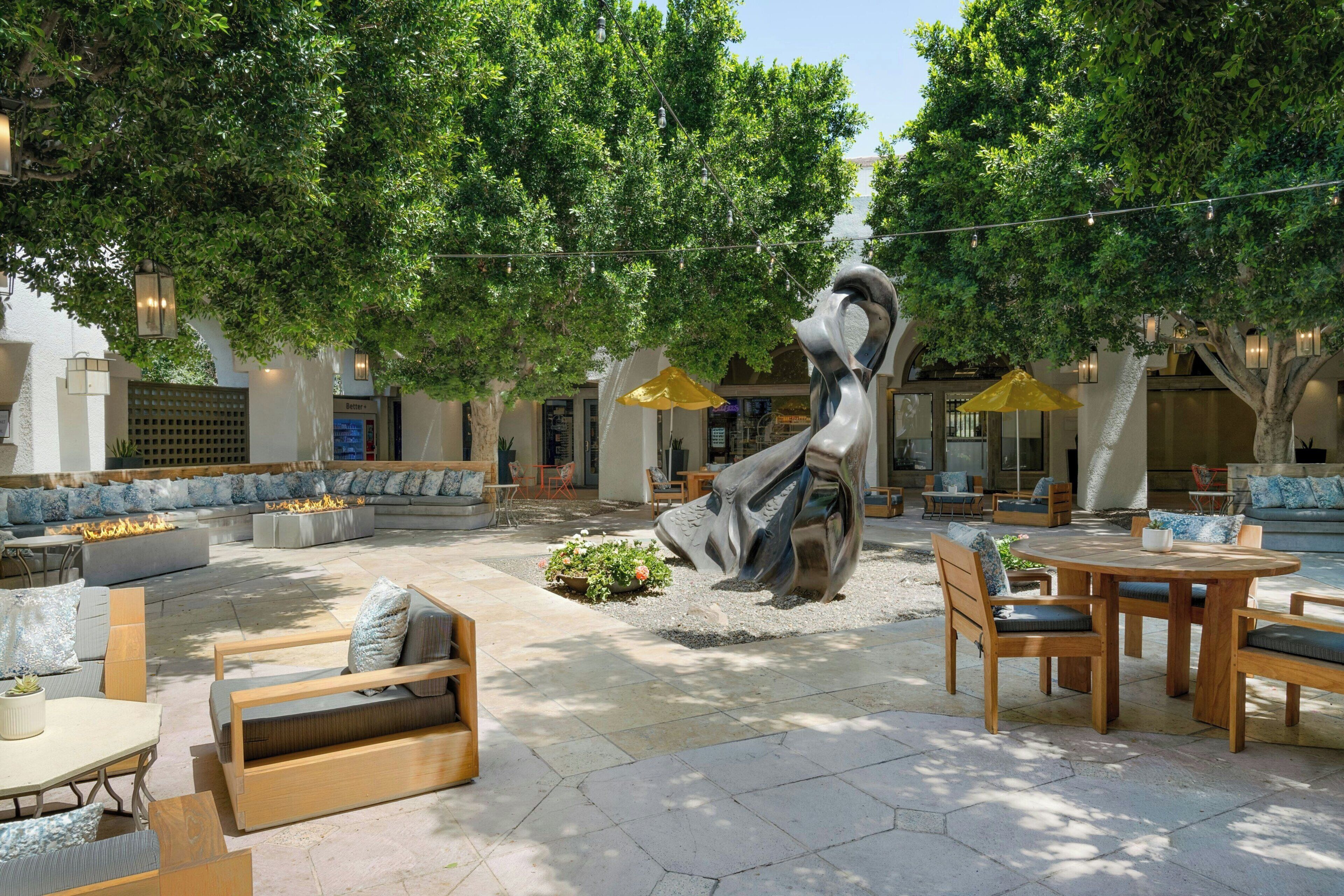 An outdoor seating area with a sculpture, wooden furniture, and a fire feature.