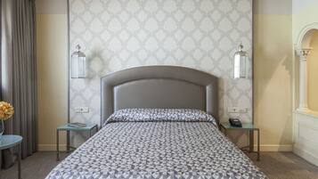 A hotel room with a patterned bedspread, two bedside tables with lamps, a vase with flowers, and a mirror on the wall.