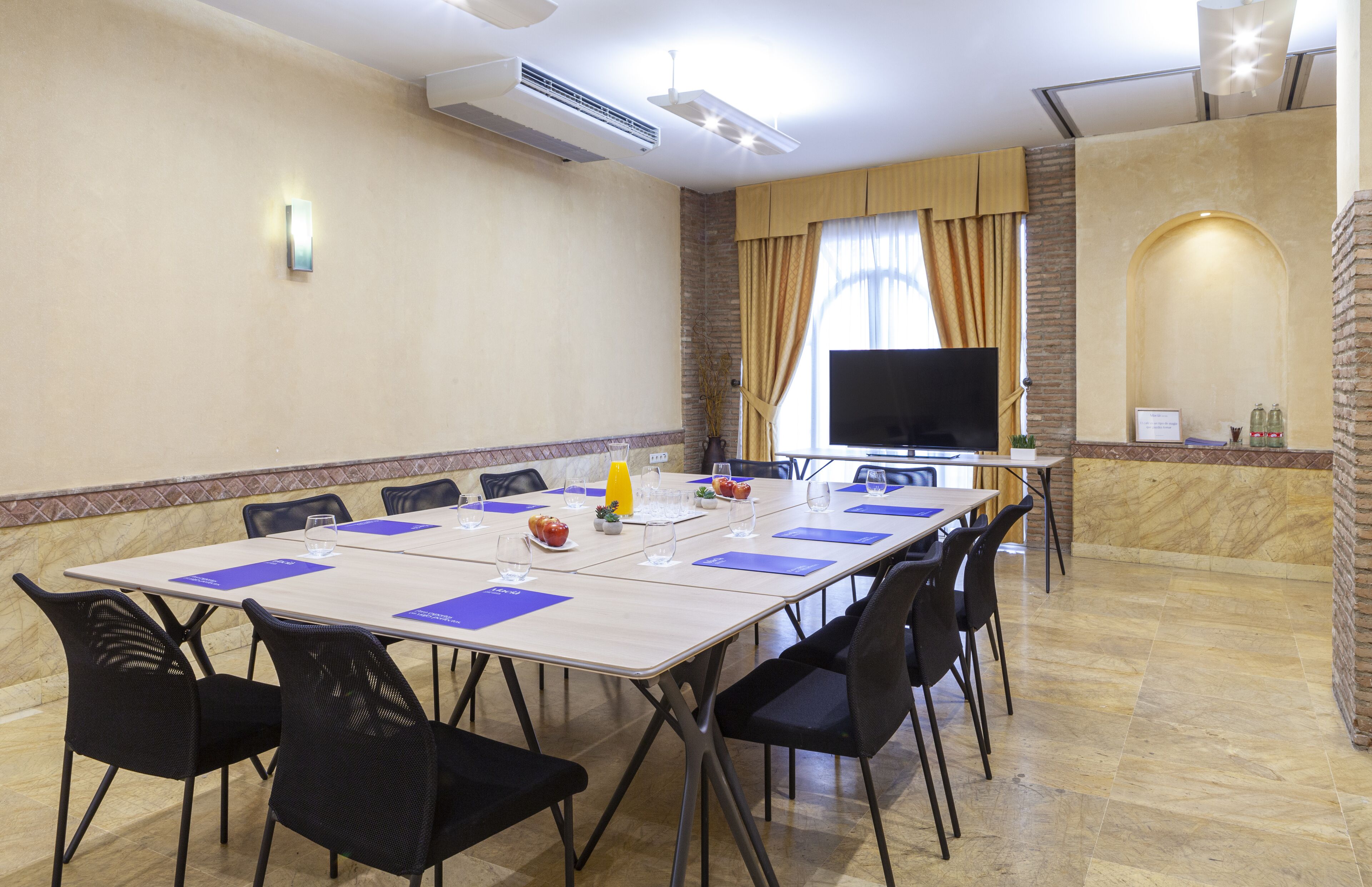 Un salón de conferencias con una mesa larga, sillas, un televisor de pantalla plana y una pared de acento de piedra.