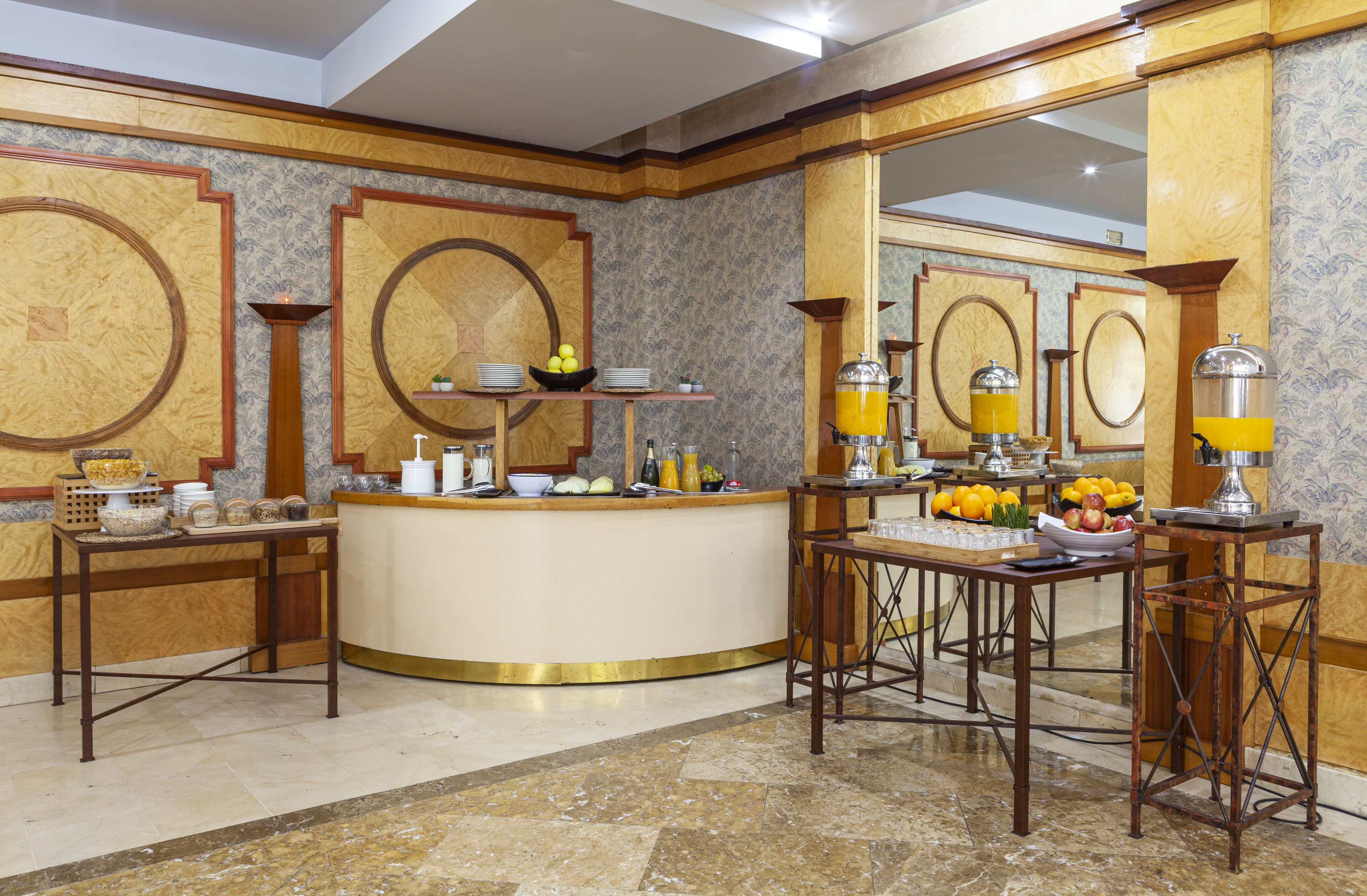 A hotel lobby with a central reception desk, a seating area with a table and chairs, and decorative wall mirrors.