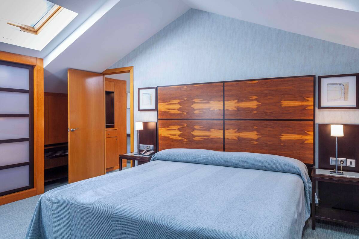 Una habitación de hotel con una cama, un armario, una mesita de noche con lámpara y un gran cabecero de madera.