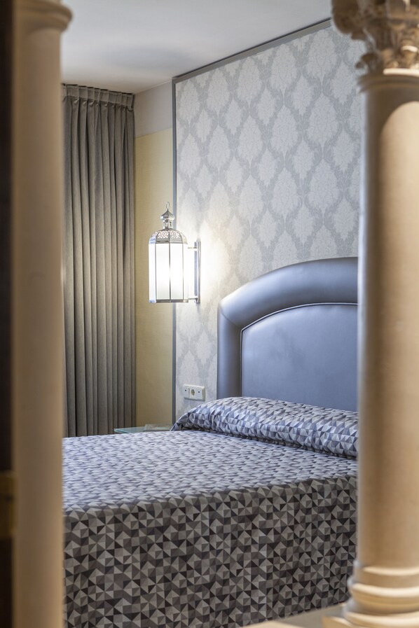 A hotel room with a bed, a wall-mounted light fixture, and a patterned wall.