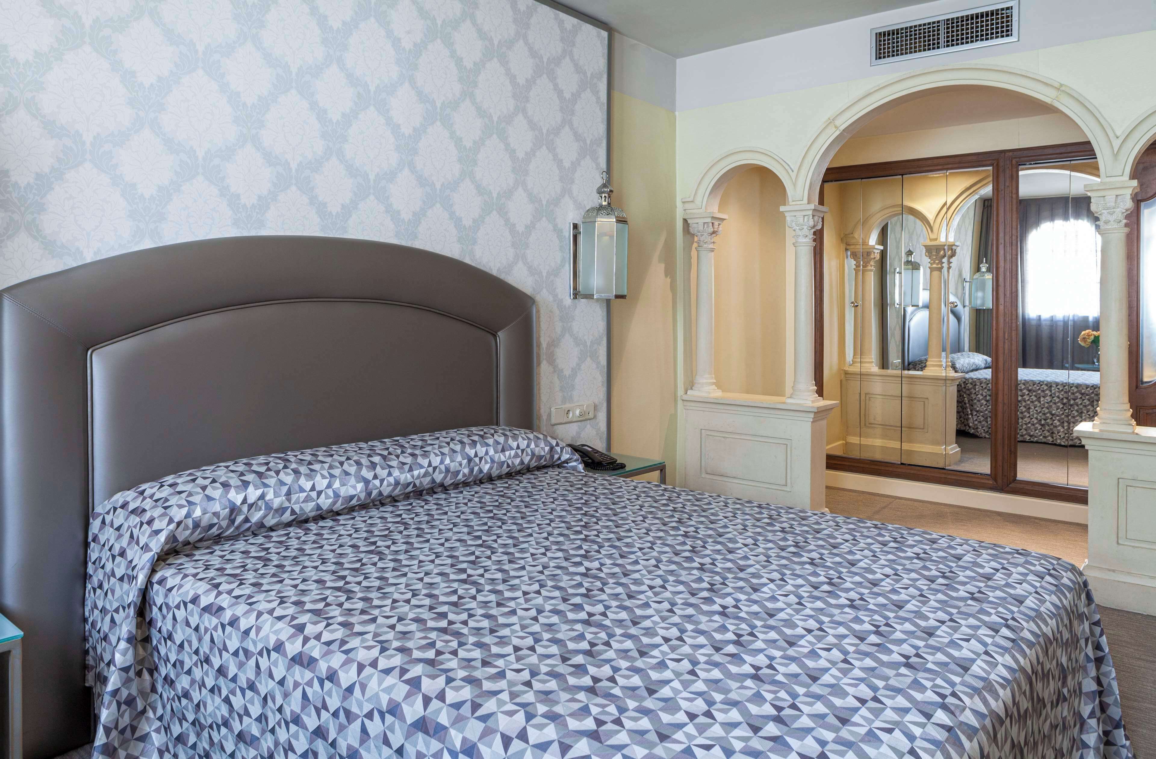 Ein Hotelzimmer mit einem großen Bett, einem Nachttisch, einem Spiegel und einem Kleiderschrank.
