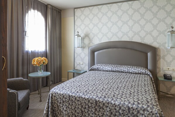 A hotel room with a large bed, a small table with a vase of flowers, a chair, and a nightstand with a lamp.