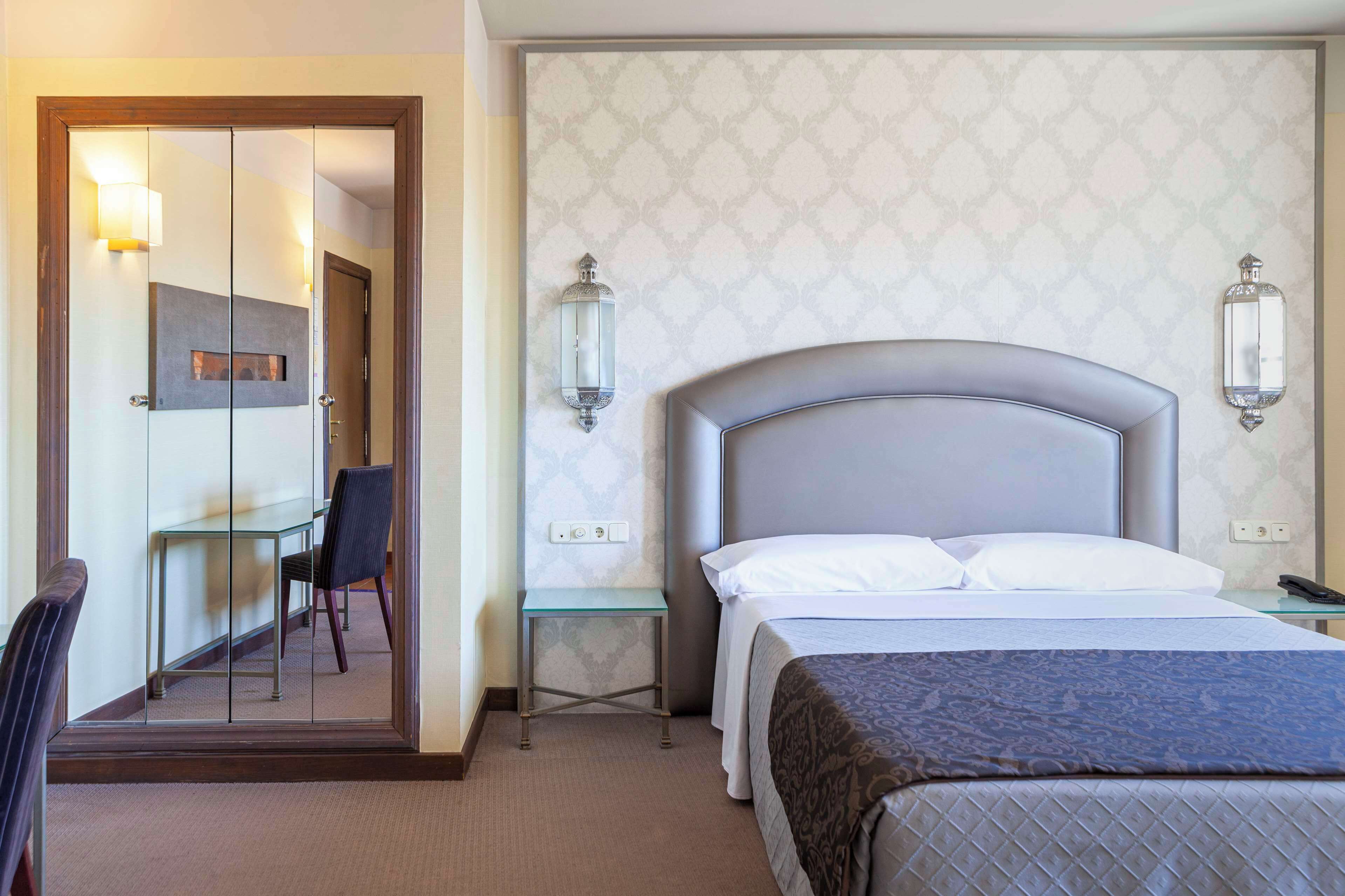 Una habitación de hotel con cama, escritorio y silla, y un espejo.