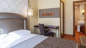 A hotel room with a bed, desk, chair, and a bathroom visible through an open door.
