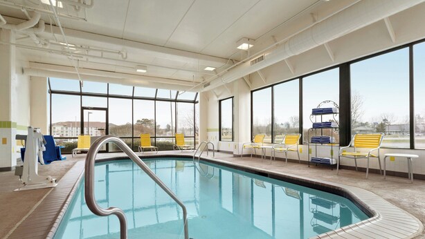 An indoor swimming pool with clear views through large windows, a pool ladder, and several yellow and white lounge chairs. - Fairfield Inn by Marriott Philadelphia West Chester/Exton (Exton)