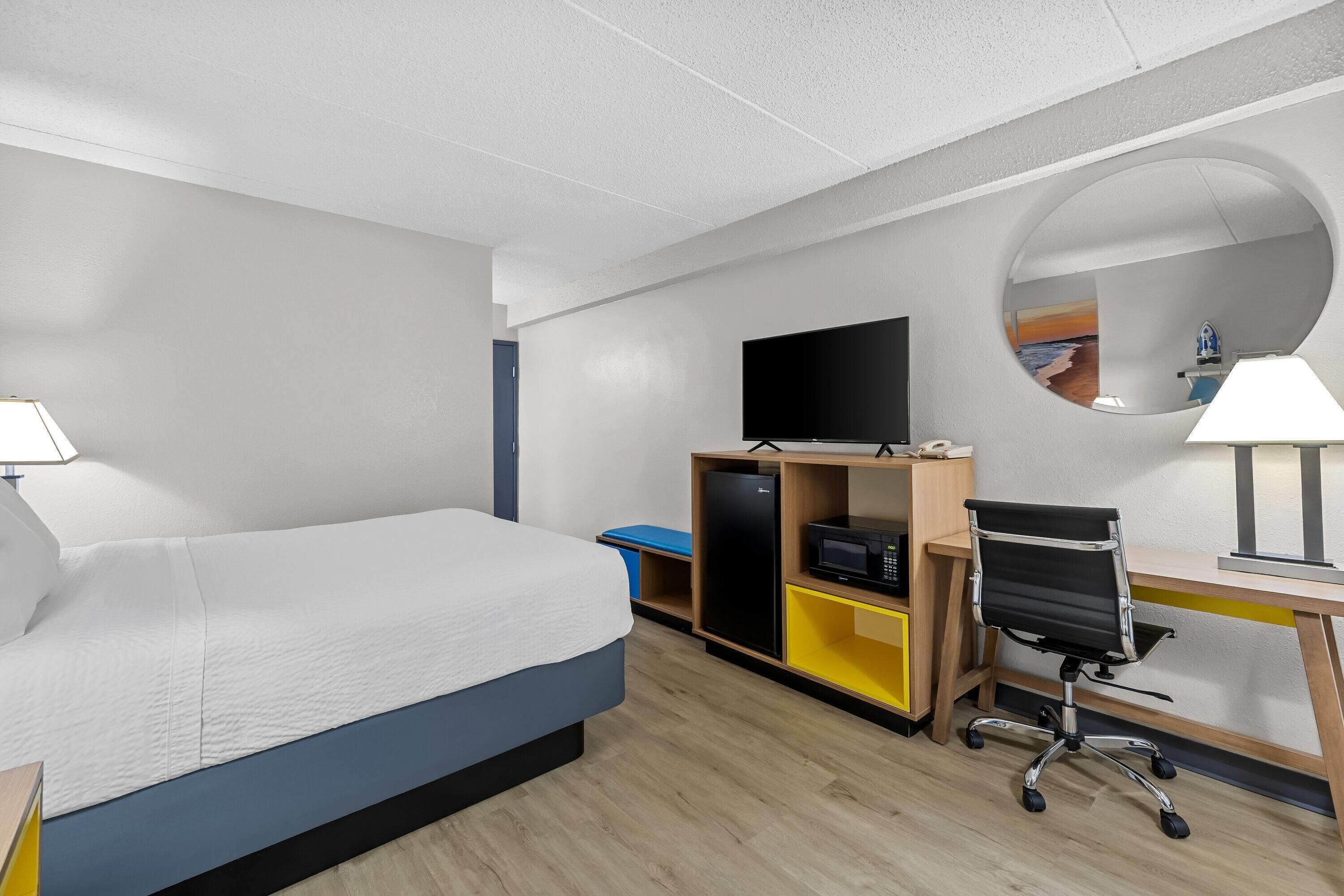 Een hotelkamer met een bed, bureau, stoel, televisie en spiegel.