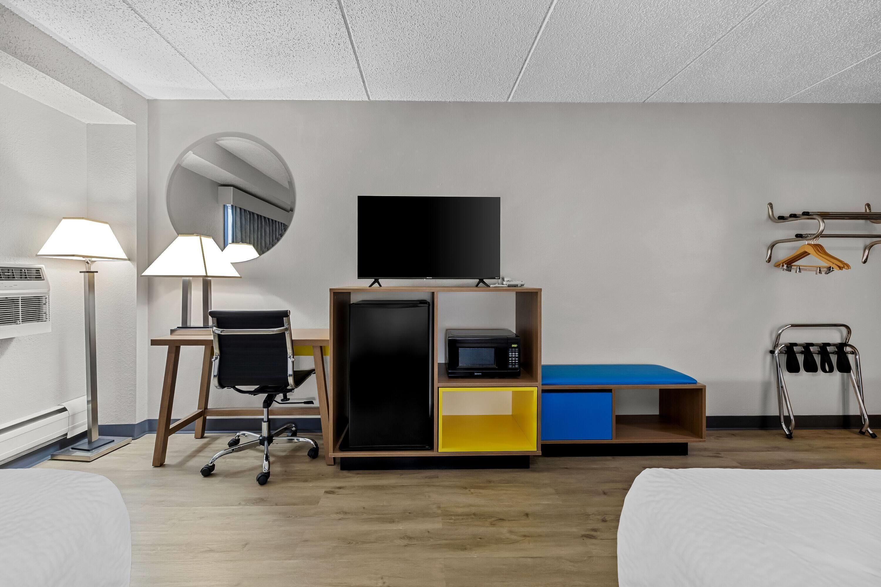 A hotel room with a bed, desk, chair, TV, microwave, and a wardrobe.