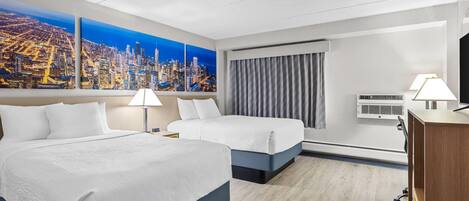 A hotel room with two beds, a cityscape view, a desk with a lamp, and an air conditioning unit.