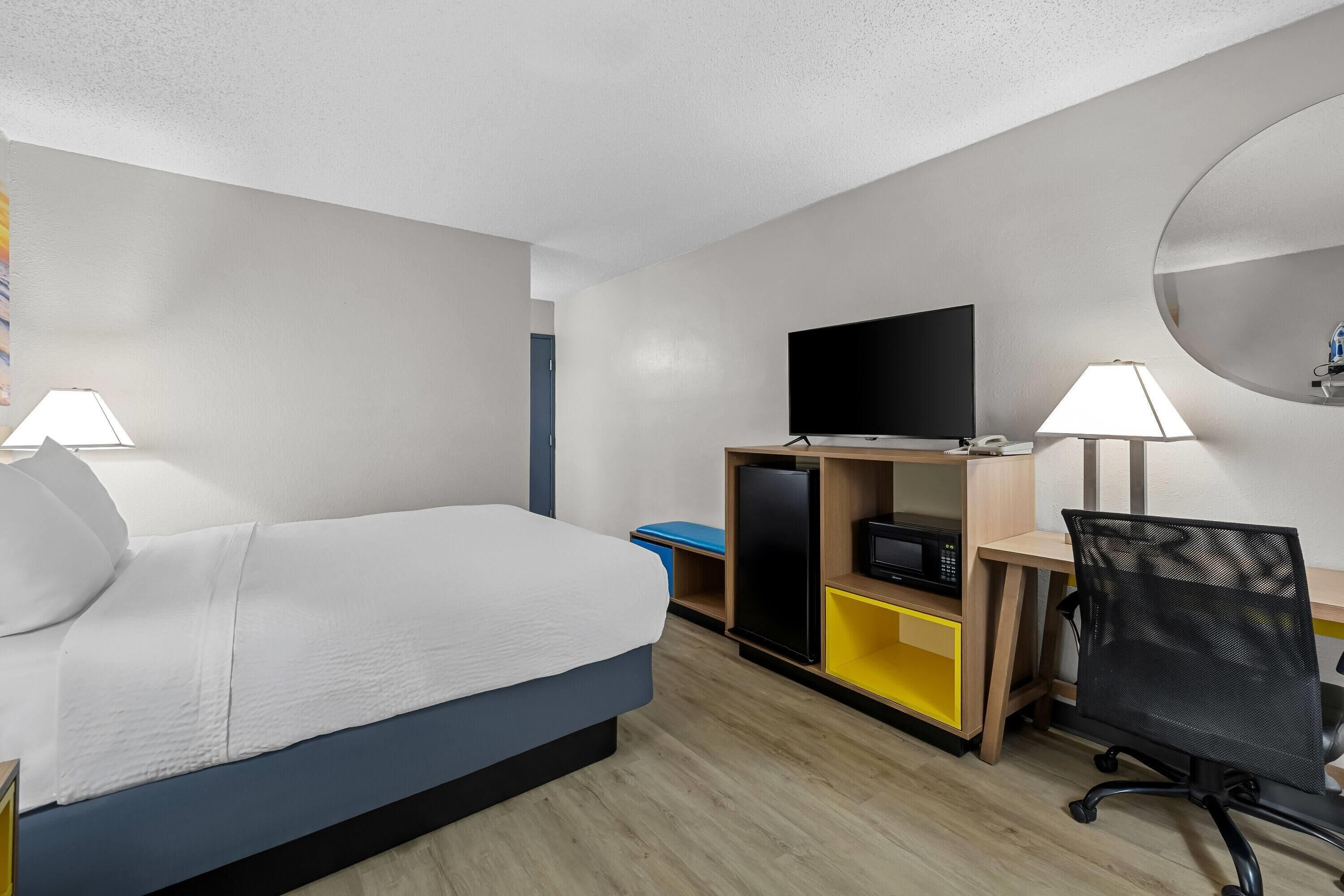 A hotel room with a bed, desk, chair, TV, and two lamps.