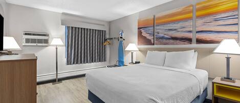 Une chambre d’hôtel avec un lit, deux lampes de chevet, un tableau représentant un coucher de soleil, un bureau et une chaise.