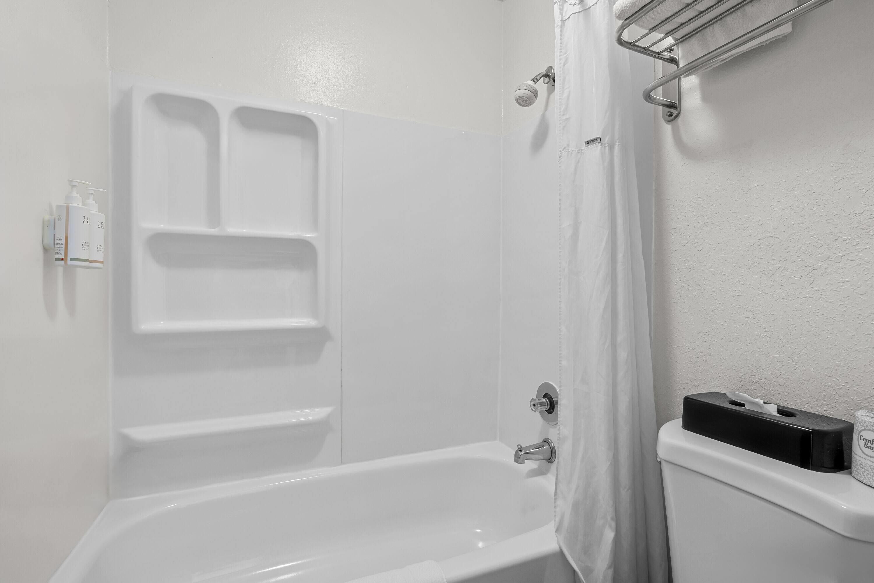 Une salle de bain avec une baignoire blanche, une douche et des toilettes. On y trouve des articles de toilette accrochés au mur et un porte-serviettes.