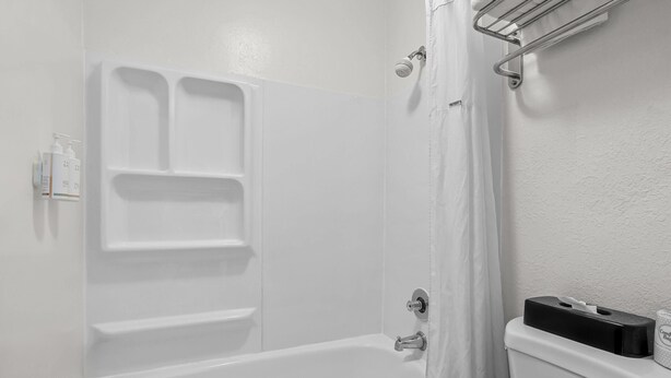 A bathroom with a white bathtub, a shower, and a toilet. There are toiletries on the wall and a towel rack.