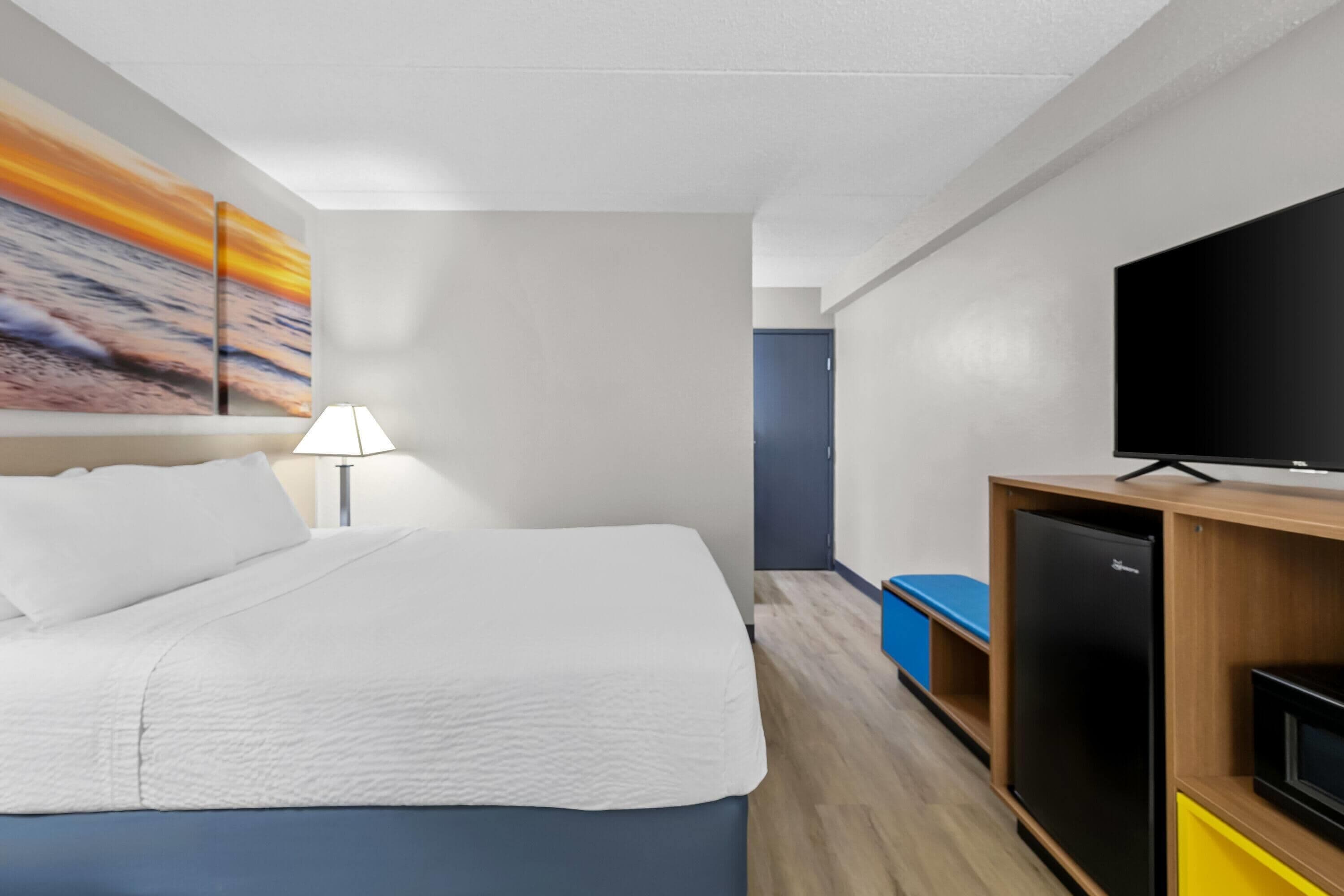 Una habitación de hotel con cama, televisor, refrigerador y un cuadro en la pared.