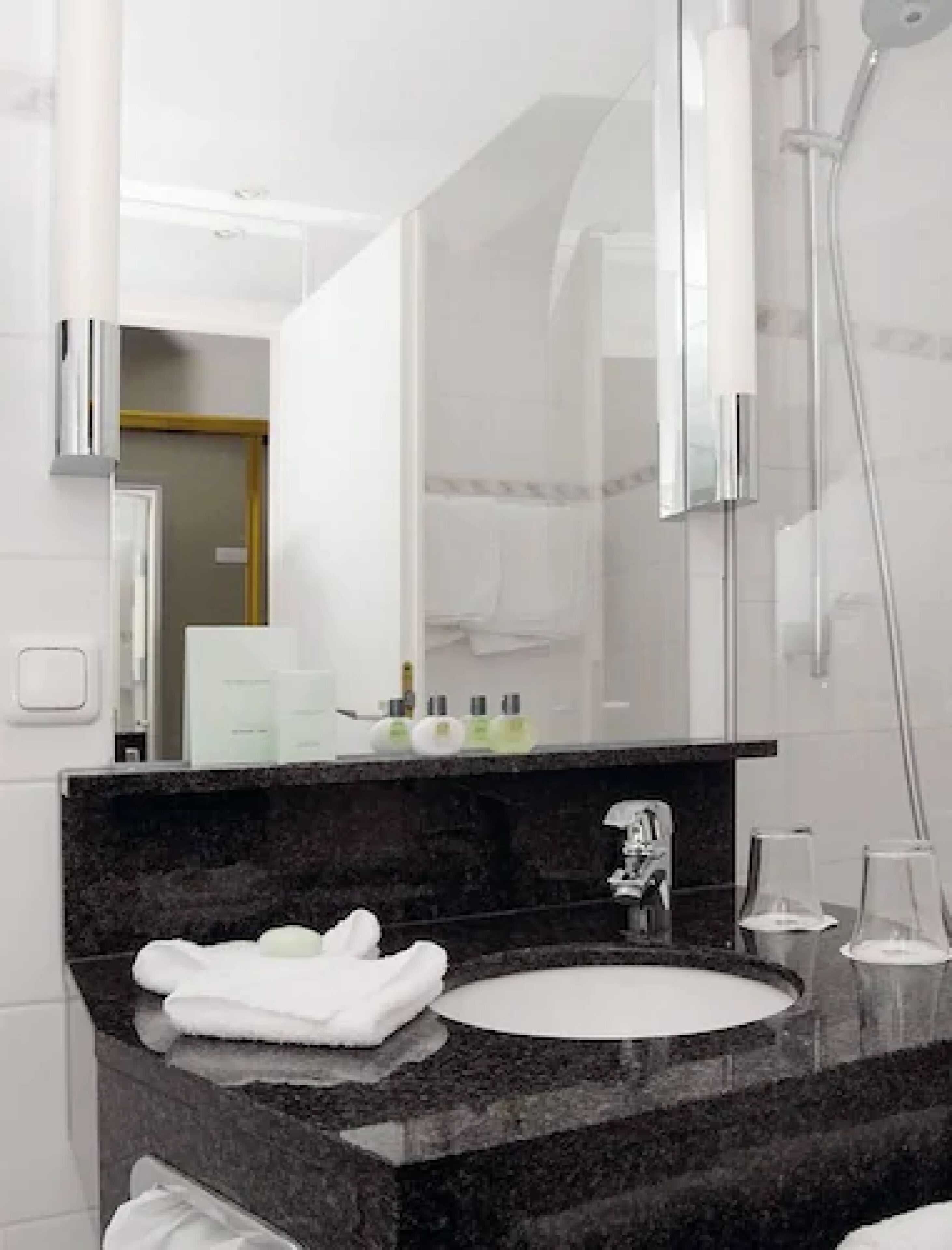 A modern bathroom with a granite countertop, a white sink, and a large mirror.