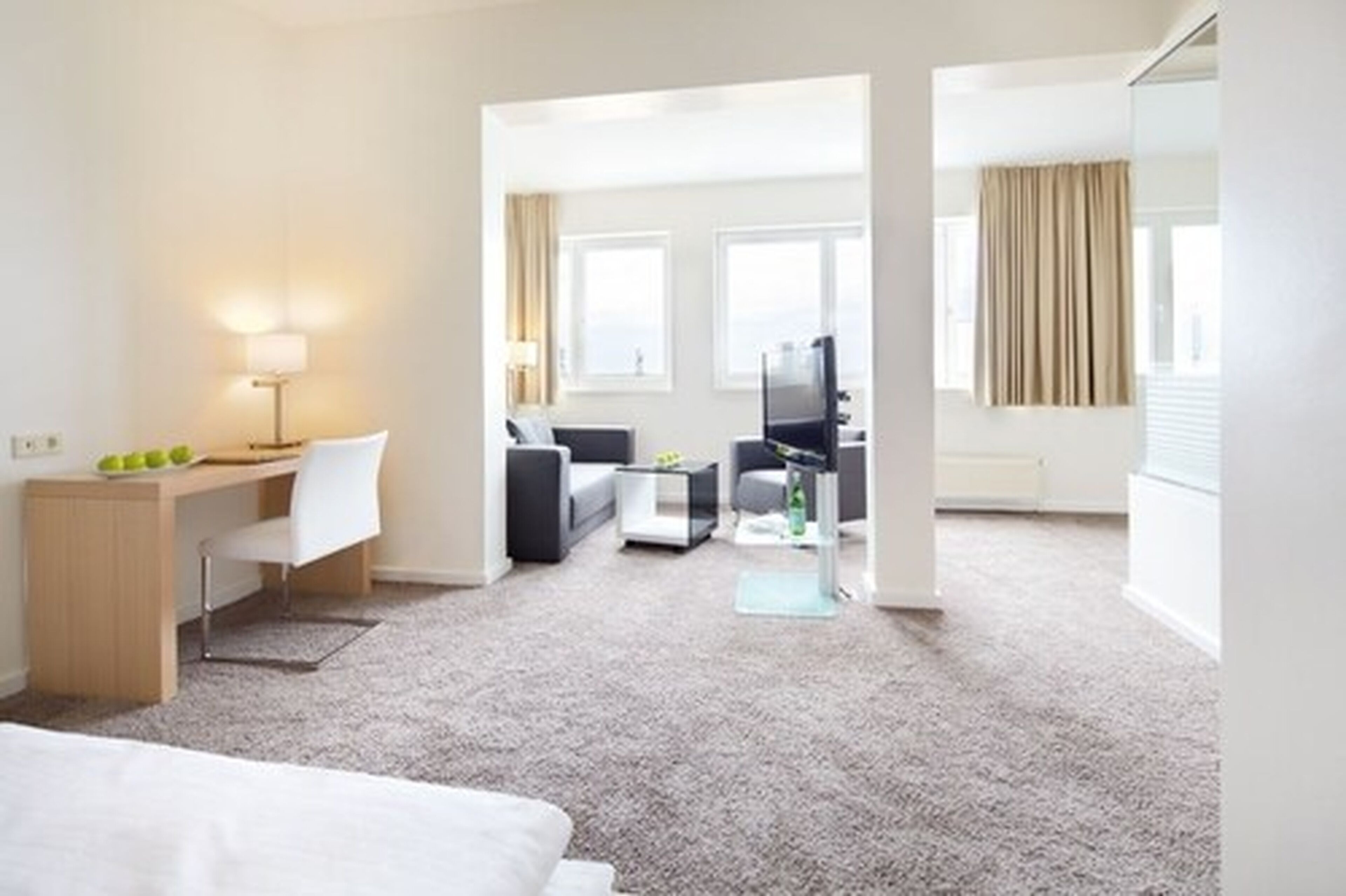 A modern hotel room with a desk, chair, sofa, and TV.