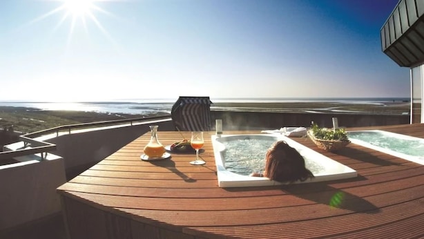 Una terraza soleada con un jacuzzi, una mesa con bebidas y vistas al océano.
