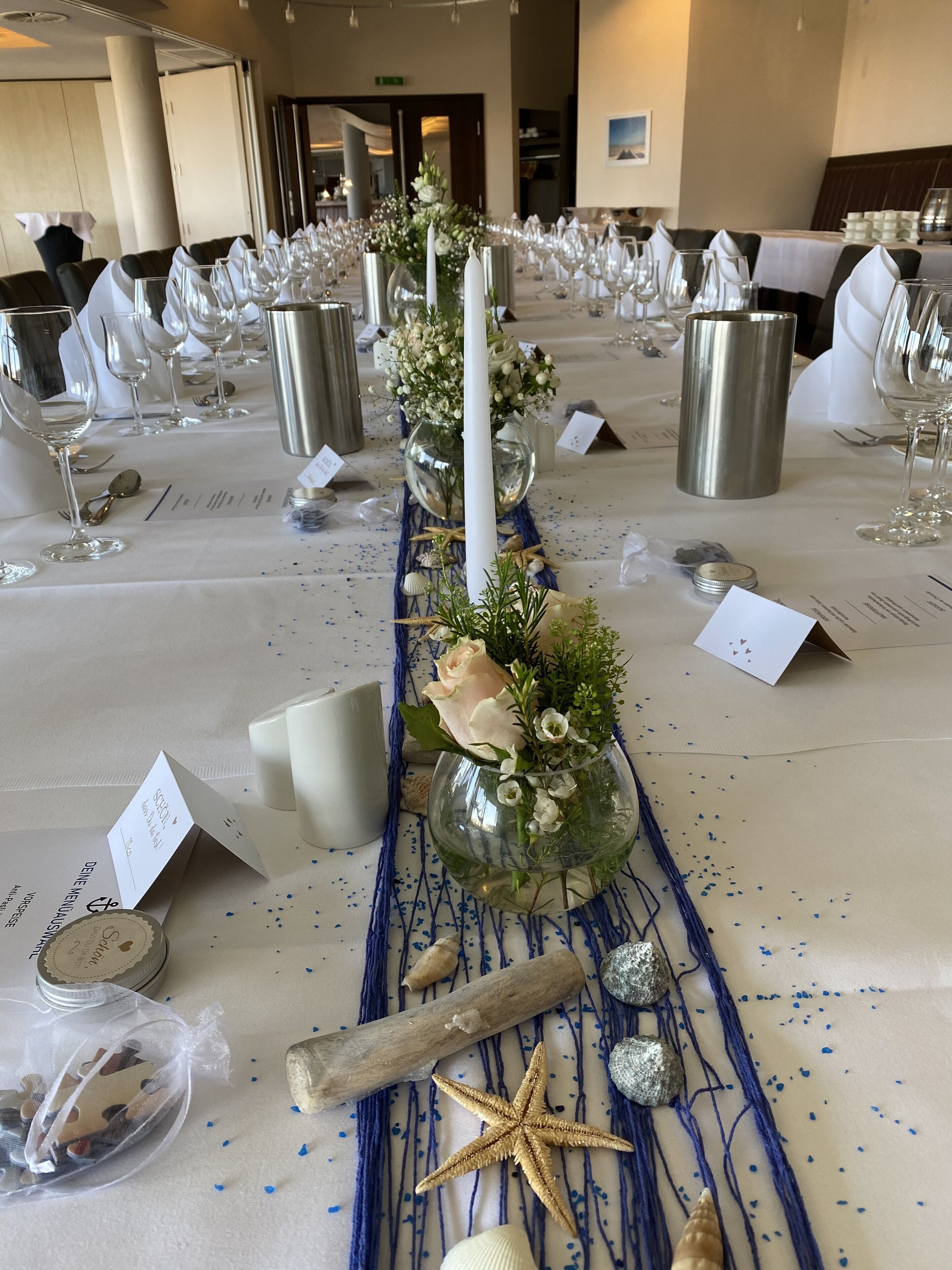 Une table de banquet dressée avec des nappes blanches, de la verrerie et des compositions florales.