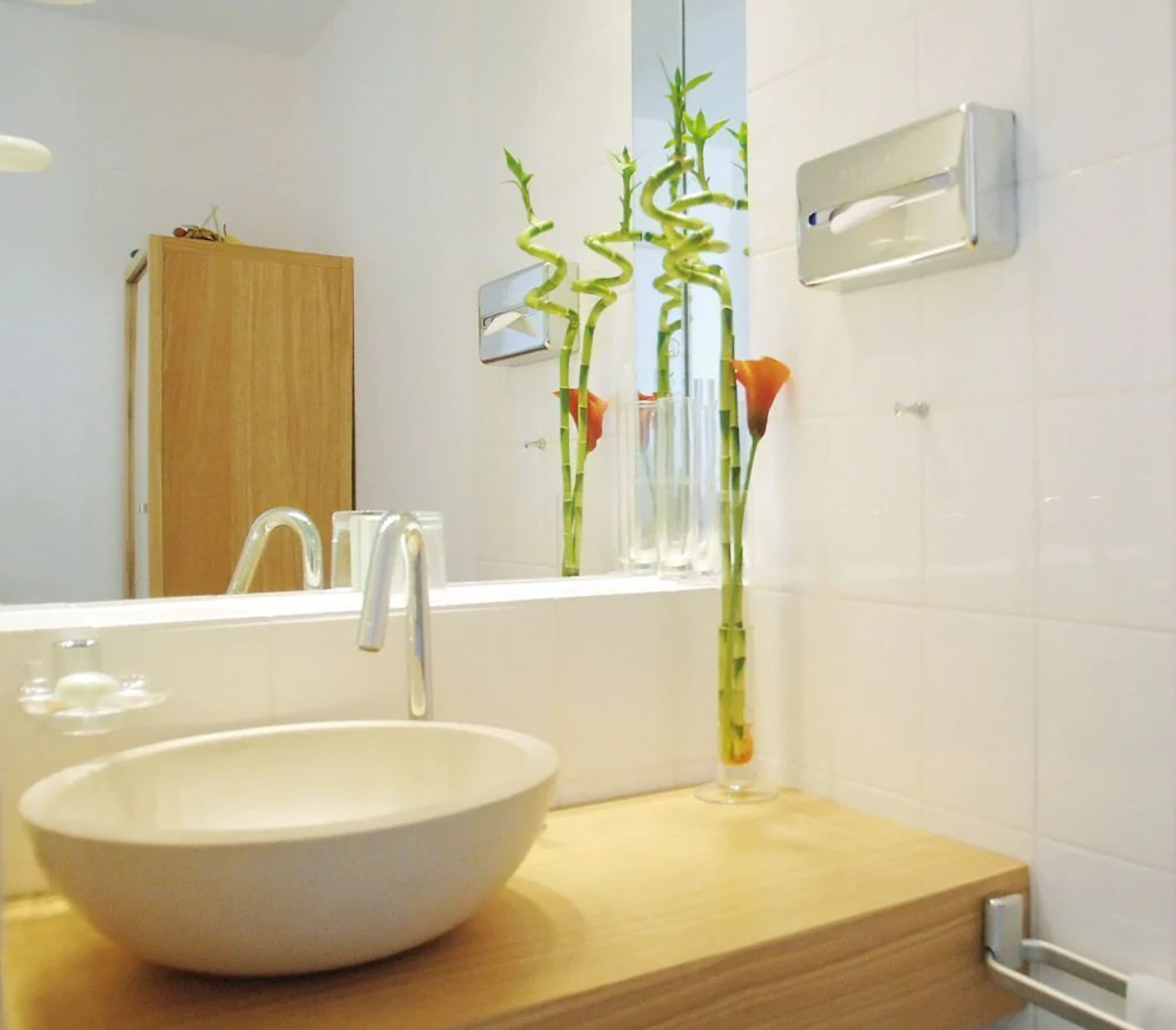 A bathroom with a white sink, a wooden vanity, a mirror, and a window with a view of bamboo plants.
