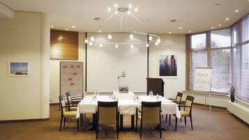 A conference room with a round table, chairs, a whiteboard, and a large window with blinds.