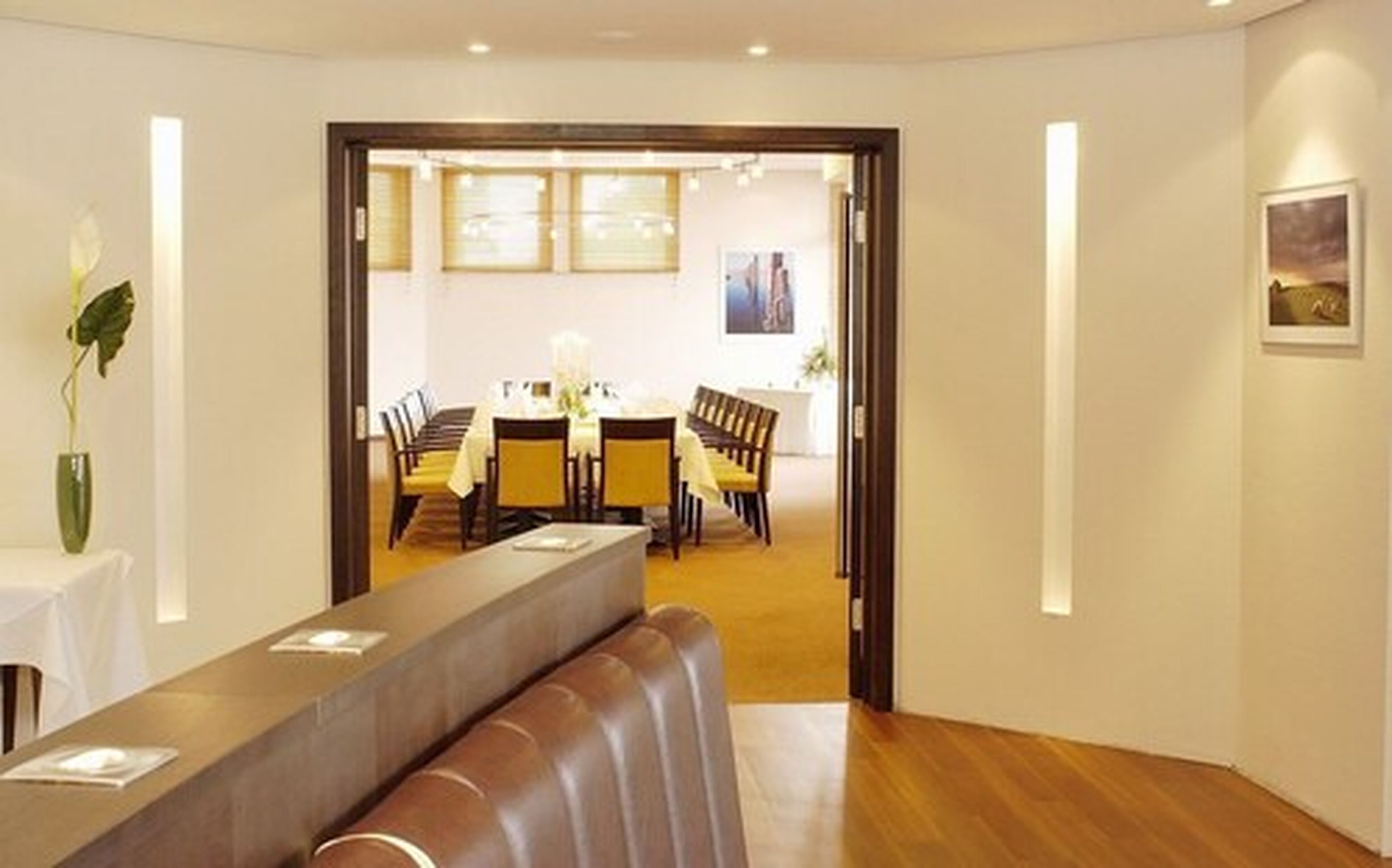 Eine moderne Hotelhalle mit einer Rezeption, einer Sitzecke und einem Essbereich, der durch eine offene Tür sichtbar ist.