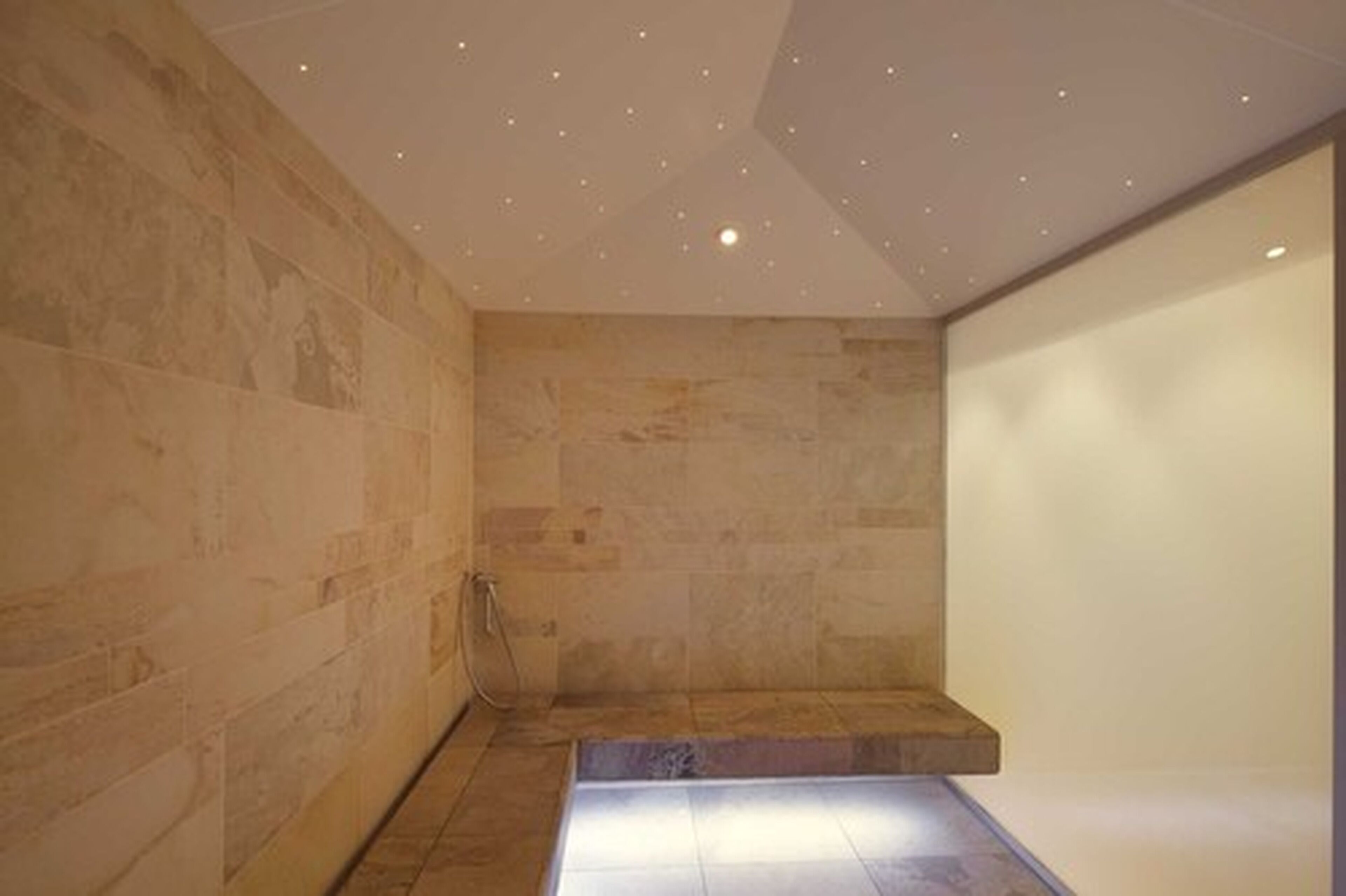 Un baño moderno con paredes de piedra, una banca empotrada e iluminación empotrada.