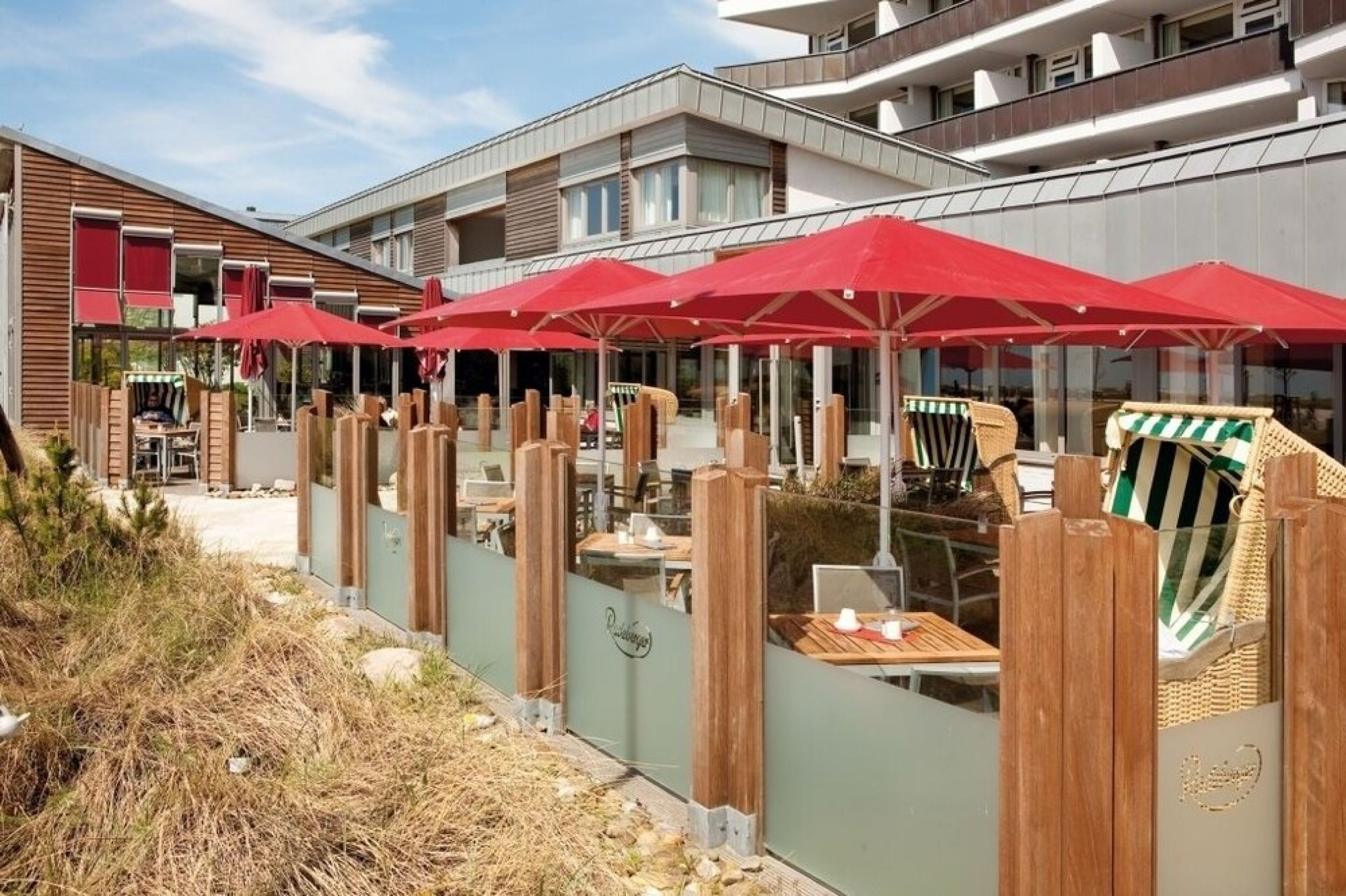 An outdoor dining area with red umbrellas, wooden chairs, and tables.