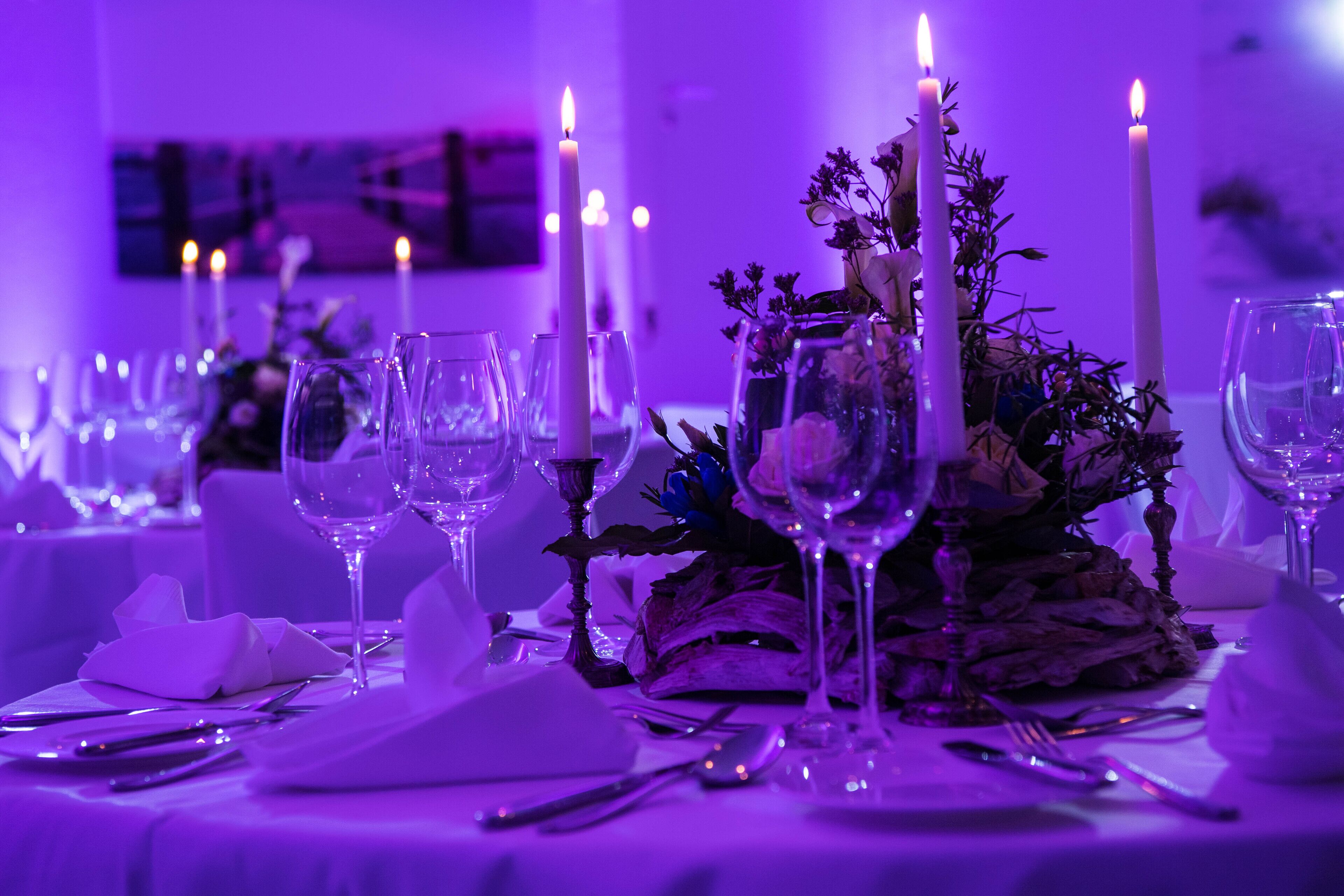 Une table dressée avec des verres à vin, des assiettes et des couverts, agrémentée de bougies et de compositions florales.