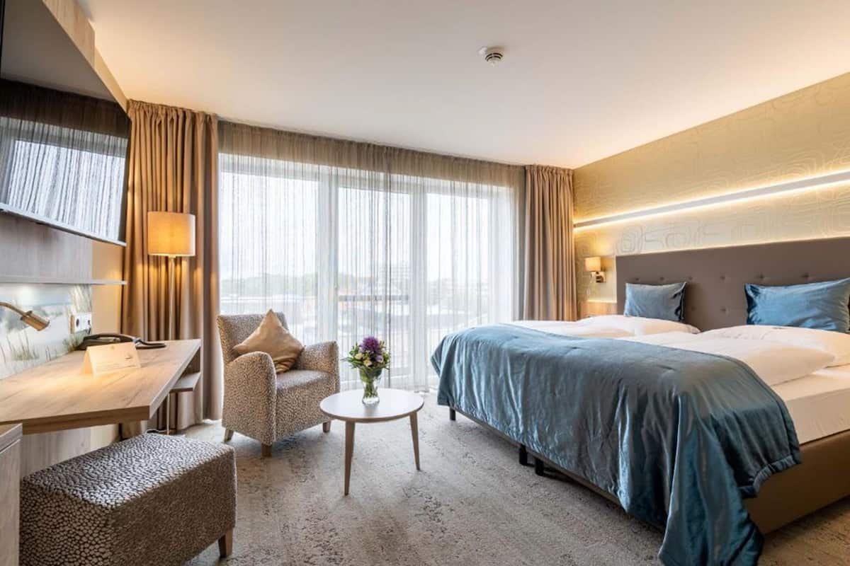 Una habitación de hotel con una cama grande, un escritorio con lámpara, una silla y una pequeña mesa con un jarrón de flores.