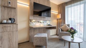 Ein modernes Hotelzimmer mit einem Holzschrank, einem Flachbildfernseher, einem kleinen Tisch mit Blumen und einem bequemen Sessel.