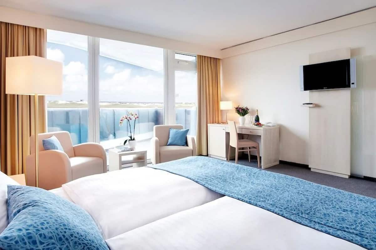 Habitación de hotel con una cama grande, un escritorio, una silla, un televisor y vistas al cielo.