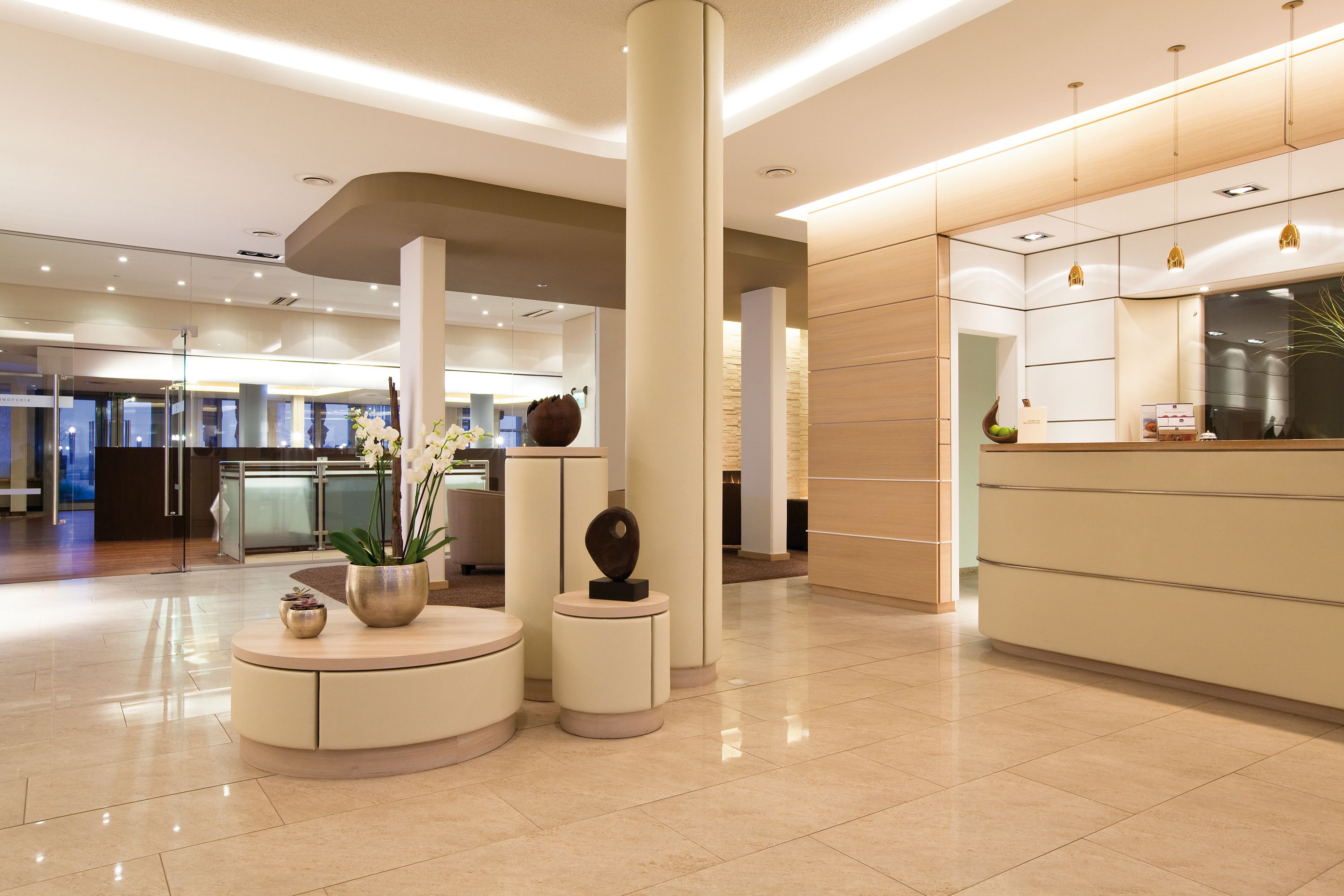 Eine moderne Hotellobby mit einer Rezeption, einer runden Sitzecke mit Blumenvase und einer großen Säule.