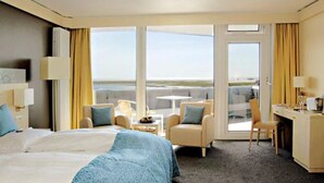 Habitación de hotel con una cama grande, dos sillones, un escritorio y vistas a la playa.