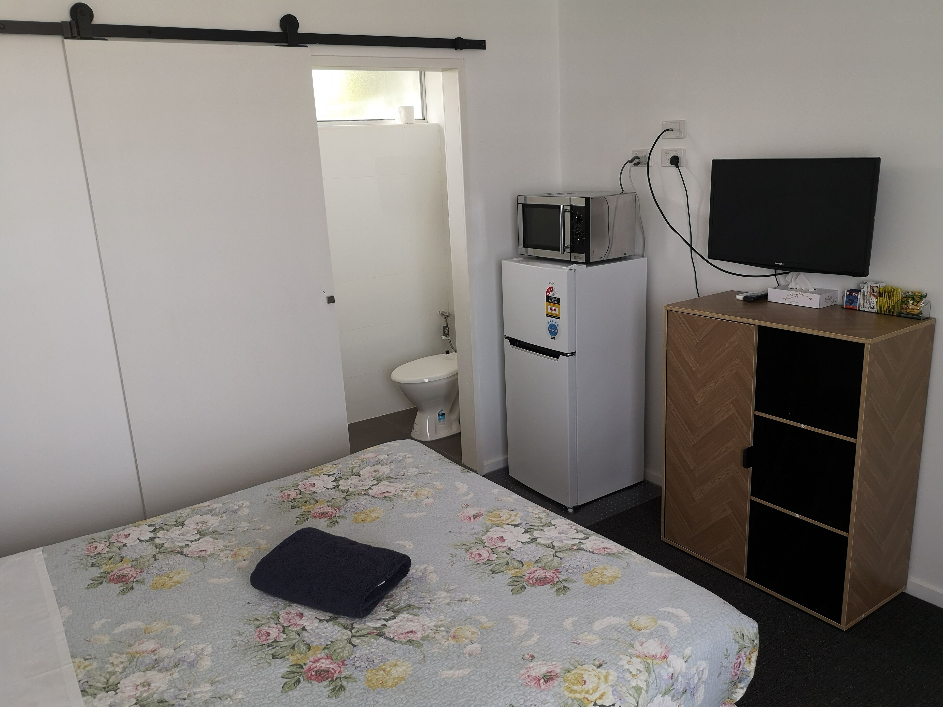 Un dormitorio con cama, armario, televisor, microondas y baño.