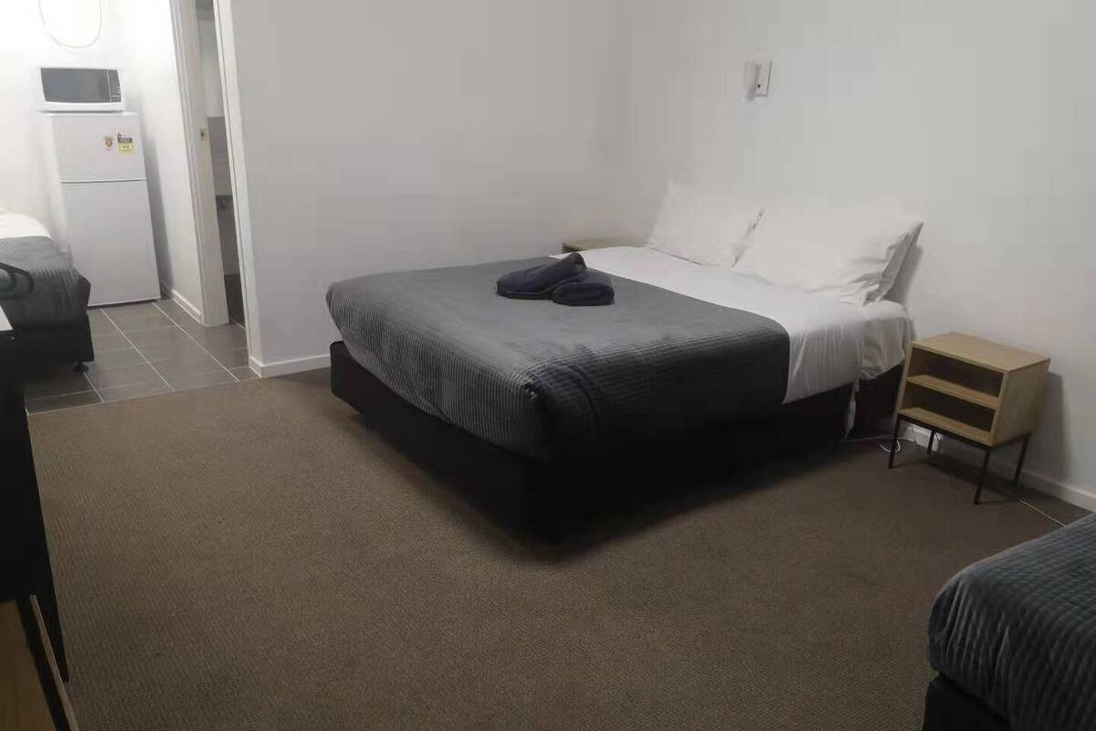 A bedroom with a bed, a nightstand, a chair, and a microwave.