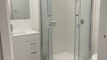 Um banheiro moderno com box de vidro, toucador branco com gavetas e vaso sanitário.