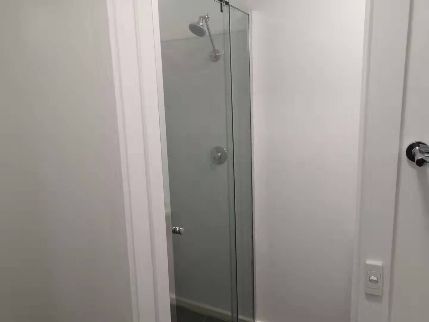 A glass-enclosed shower stall with a handheld showerhead and a door with a silver handle.