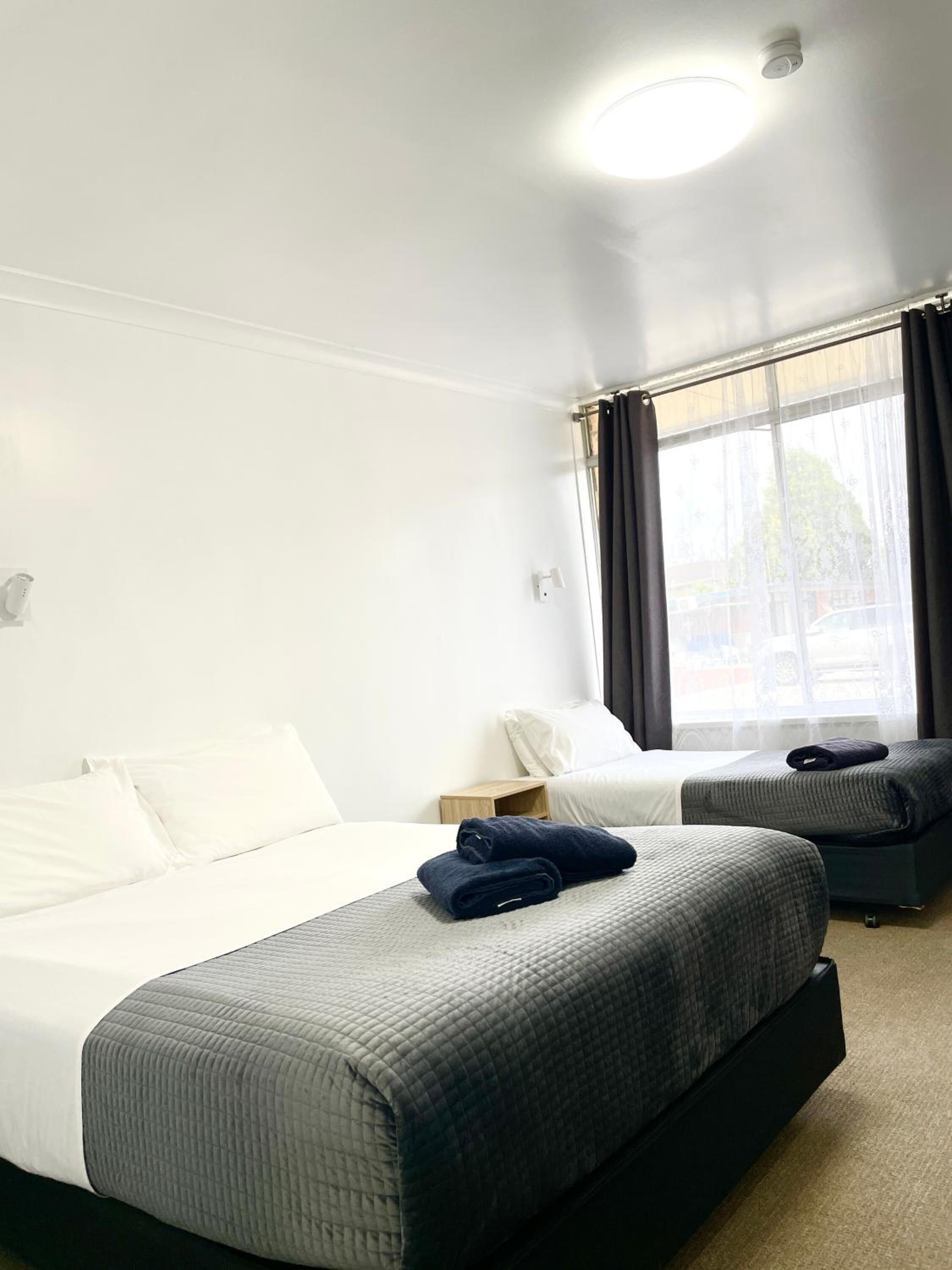 A hotel room with a large bed, a smaller bed, a nightstand, and a window with curtains.