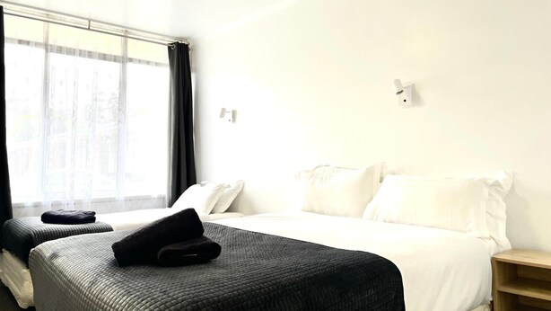 Et hotelværelse med en seng, to sengeborde, et vindue med gardiner og en lampe monteret på væggen.