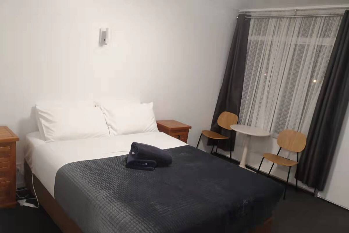 A hotel room with a bed, a small table, two chairs, and a window with curtains.