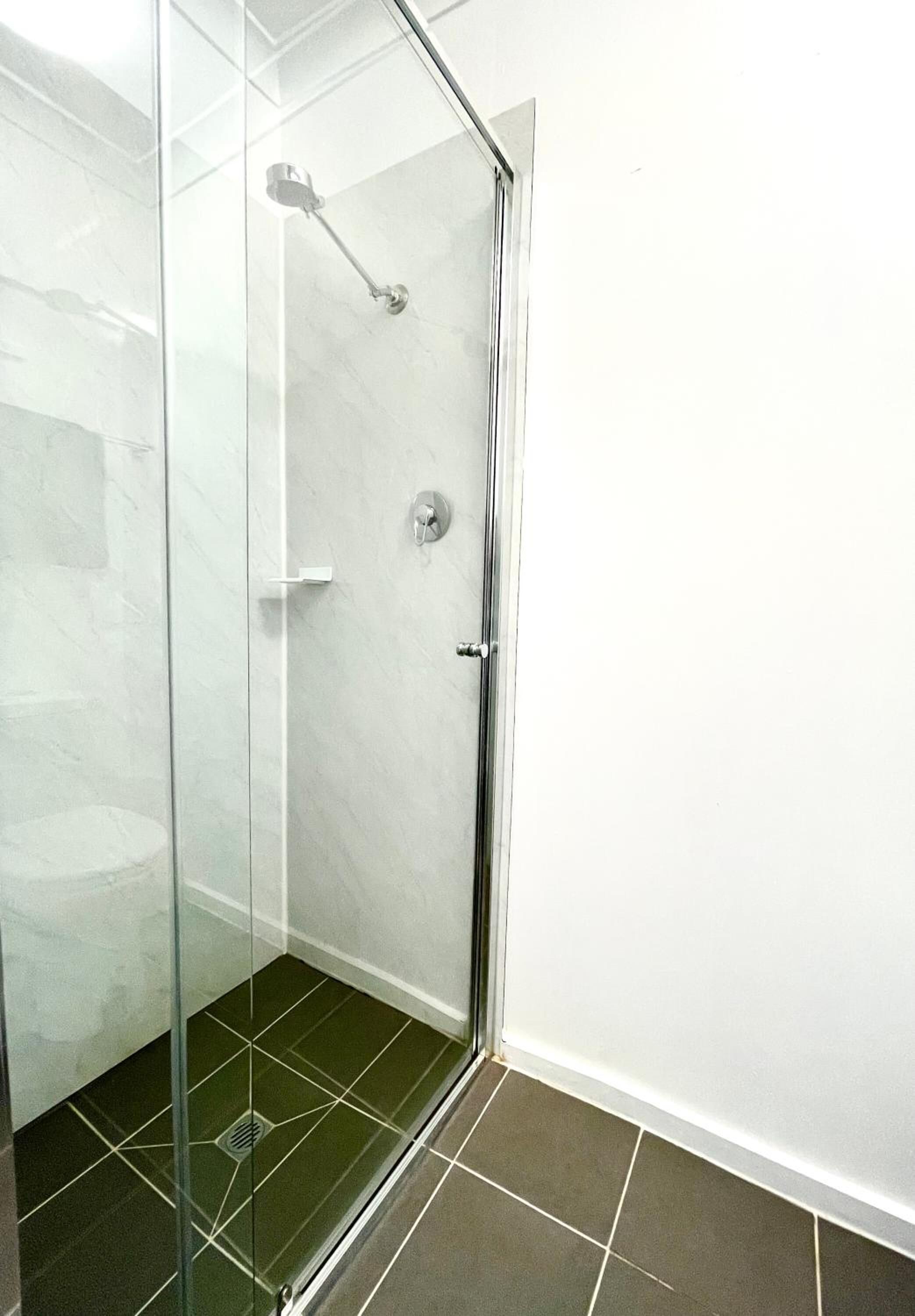 A glass-enclosed shower with a handheld showerhead, a wall-mounted control panel, and a tiled floor.