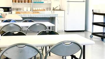 A clean, modern kitchen with white cabinets, a refrigerator, and a sink. There are several chairs and a table in the foreground.