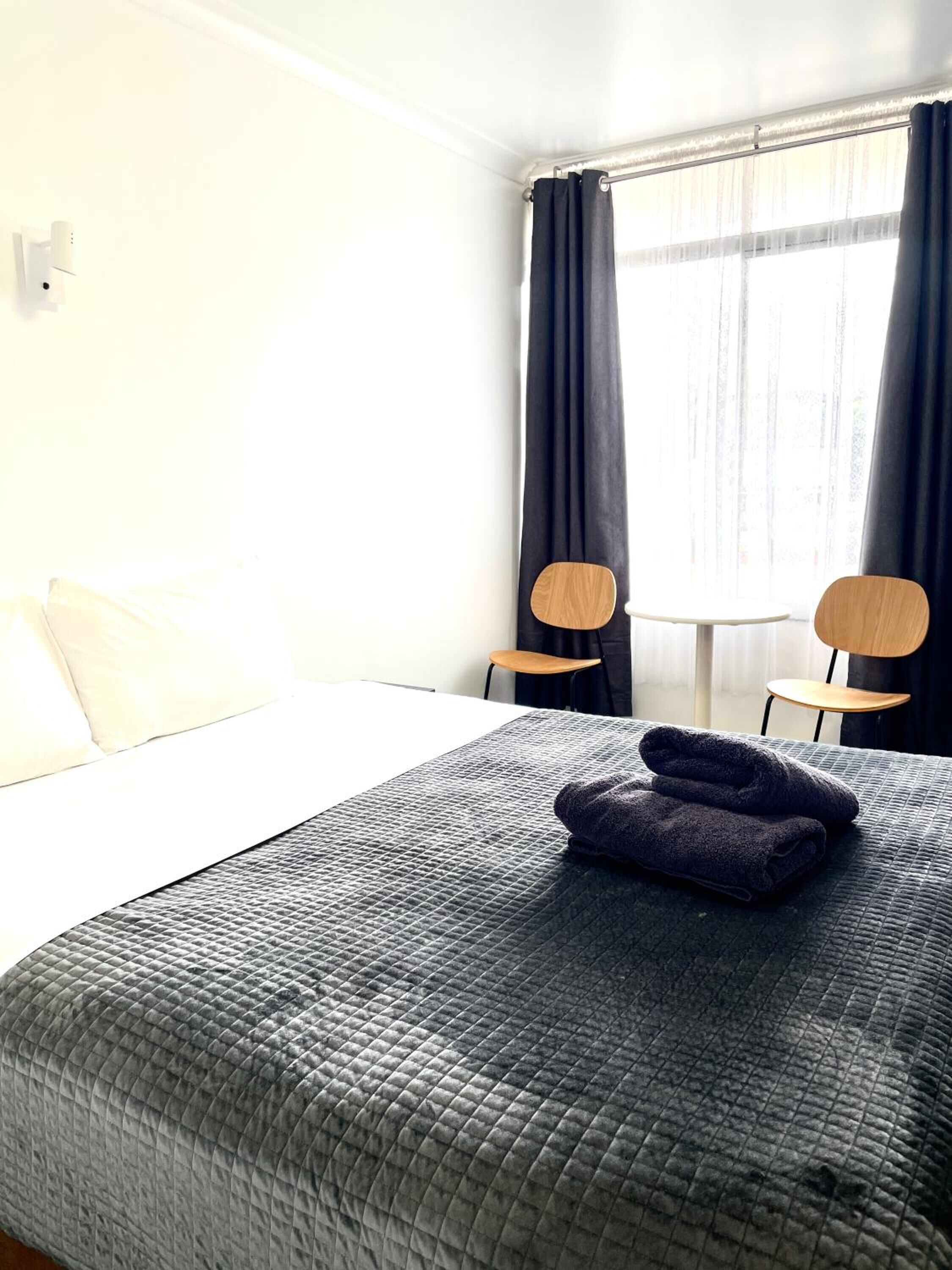 A hotel room with a bed, two chairs, a small table, and a window with curtains.