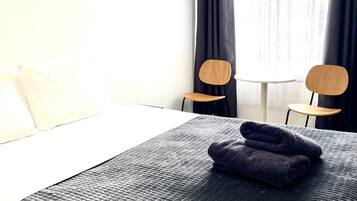 A hotel room with a bed, two chairs, a small table, and a window with curtains.