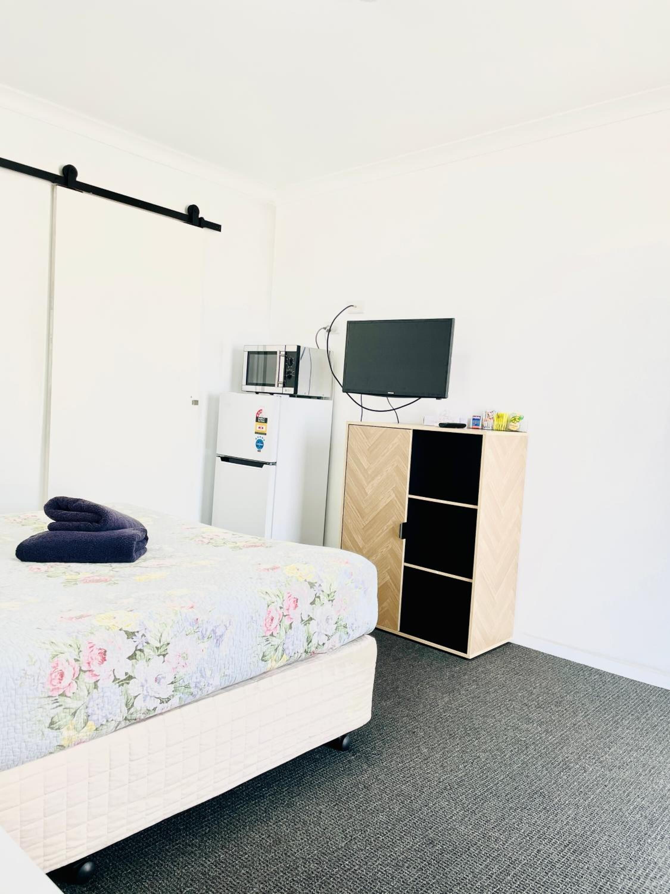 A hotel room with a bed, a flat-screen TV, a microwave, and a wooden wardrobe.