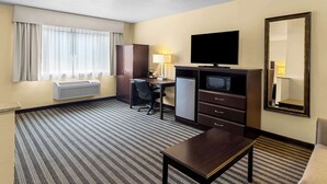 A hotel room with a bed, a desk, a television, a microwave, a refrigerator, a chair, and a large mirror. - Quality Inn & Suites Vancouver - Hazel Dell (Vancouver)