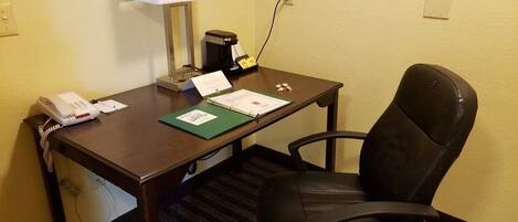 A hotel room with a wooden desk, a black leather chair, a lamp, a phone, and a coffee maker.