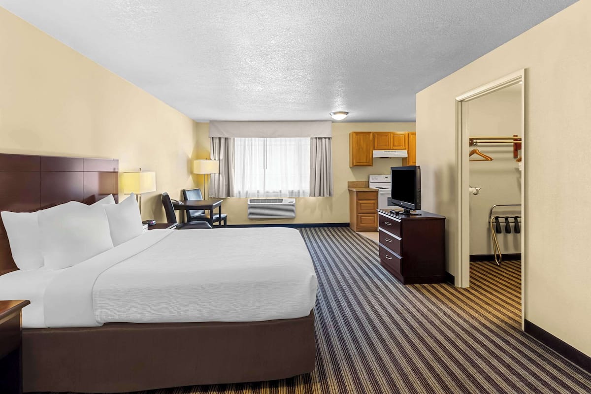 A hotel room with a large bed, a desk with a chair, a television, a wardrobe, and a bathroom visible through an open door.
